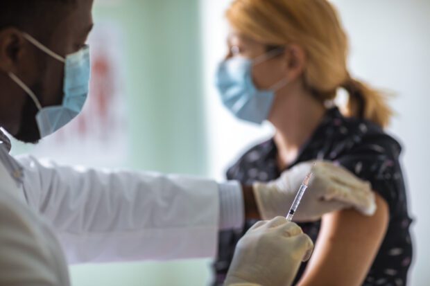 Doctor with face mask administering vaccination to female patient